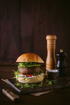 a hamburger sitting on top of a cutting board next to a knife and pepper shaker