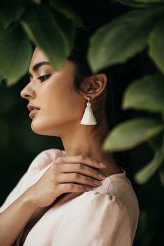 a woman wearing white earrings and a pink dress is standing in front of some green leaves