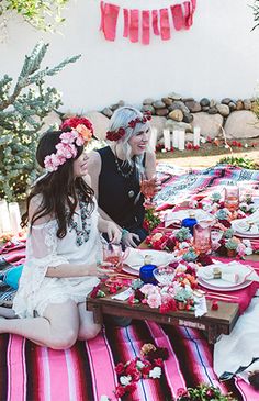 two women sitting on the ground with food and drinks in front of them, all dressed up