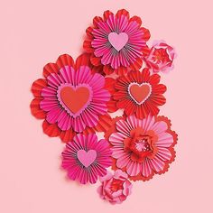 pink and red paper flowers with hearts cut out of them on a pink background for valentine's day