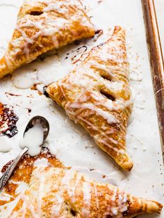 three pieces of pastry with icing and spoons on a baking sheet, ready to be eaten