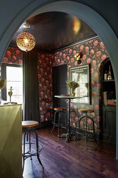 an arched doorway leads to a bar with floral wallpaper on the walls and wooden floors