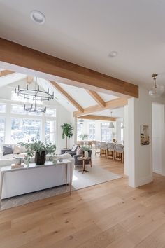 a living room filled with furniture and a large window next to a kitchen area covered in wooden beams