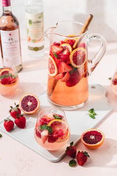 a pitcher filled with liquid and garnish next to sliced strawberries on a plate