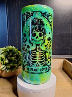 a green candle with a skeleton on it sitting next to a potted succulent