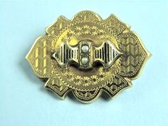 "Very pretty 18k gold pin from the mid Victorian Period c. 1870 is formed of a hollow shield-shaped body etched with a wavy pattern, tiny star bursts and decorative trim.  The top has a stylized ribbon surmounted that is decorated with taille d'Epergne enameling and is set with two grey seed pearls.  This is a fine example of the etching that was typical of the period.  The back has a C-clasp and tube hinge and also has a hole that likely held a hook or loop to have it serve as a pendant.  Measu Ornate Engraved Yellow Gold Brooches, Ornate Gold Locket Brooches, Victorian Engraved Medallion Brooches, Victorian Gold Engraved Brooches, Victorian Engraved Gold Brooches, Ornate Gold Engraved Brooches, Victorian Gold Brooch With Screw Back, Wavy Pattern, Gold Pin