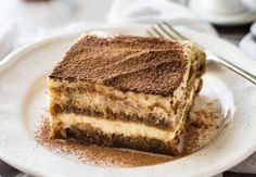 a piece of tirami cake on a white plate with coffee in the background