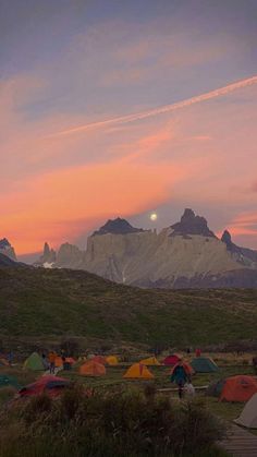 a group of tents set up in the grass with mountains in the background at sunset