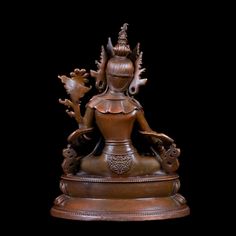 a bronze statue sitting on top of a wooden table next to a black background,