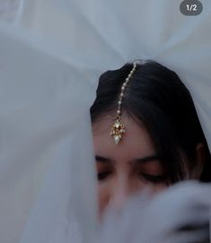 a woman wearing a white veil with a gold head piece on her head and pearls in the hair