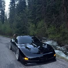 a black sports car parked on the side of a road next to a river and trees