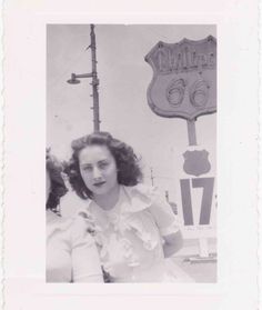 an old black and white photo of a woman standing in front of a neon sign