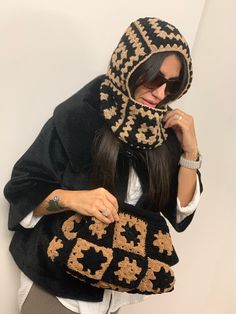 a woman wearing a black and gold knitted hat holding a handbag in her hands