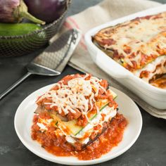 two white plates with lasagna casserole on them next to a basket of vegetables