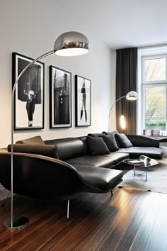 a modern living room with black leather couches and pictures on the wall above it