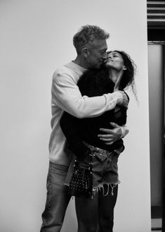 a man and woman kissing each other in front of a white wall with the door open