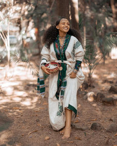 a woman walking through the woods holding a bowl