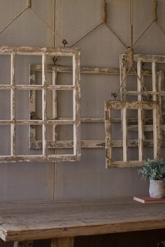 two old window frames hanging on a wall next to a table with a potted plant