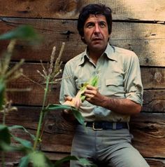 a man sitting on top of a bench next to a wooden wall holding a plant