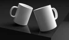 two white coffee mugs sitting on top of a black table next to each other