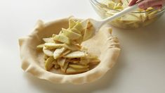 a person scooping apples out of a pie crust in a bowl with a plastic spoon