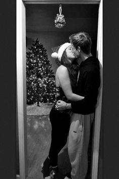 a man and woman kissing in front of a christmas tree with a santa hat on