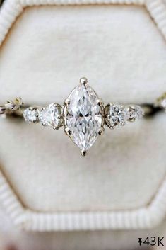 an engagement ring with three pear shaped diamonds on it, sitting in a white velvet box