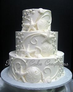 a three tiered white wedding cake with pearls and seashells on the side