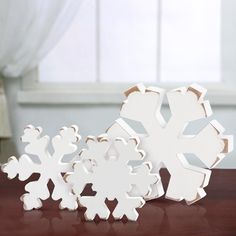 three snowflakes sitting on top of a wooden table next to a white window