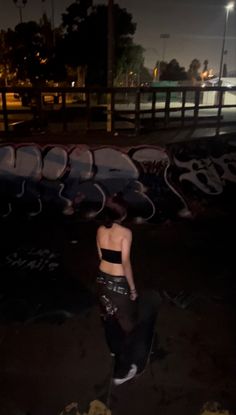 a woman standing in front of a wall covered in graffiti at night with her back turned to the camera