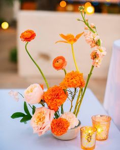 an arrangement of flowers in a vase on a table with candles and votives