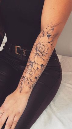 a woman with a flower tattoo on her left arm and hand is sitting on a bed