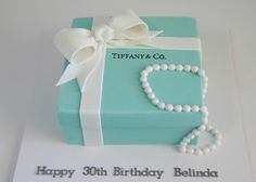 a birthday cake that is shaped like a gift box with pearls and a necklace on it