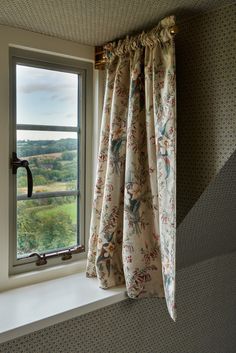 a window with curtains hanging from it's side in front of a wallpapered wall