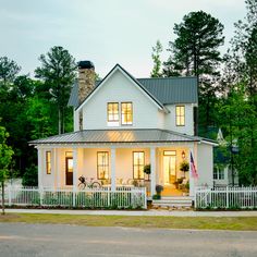 a large white house with a porch and two windows on the front, surrounded by trees