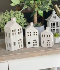 three white ceramic houses sitting on top of a table next to a potted plant