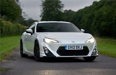 a white toyota sports car driving down a road next to some grass and trees in the background