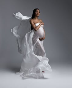 a pregnant woman in a white dress with flowing fabric around her waist and belly, posing for the camera