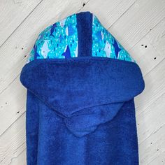 a blue towel is laying on the floor next to a white wooden wall and it's hood up