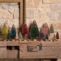 small christmas trees are lined up on a table in front of a framed mirror and stone wall