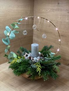 a candle sits in a wooden bowl with greenery and lights on the table next to it