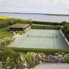 an aerial view of a tennis court surrounded by flowers and greenery with the ocean in the background