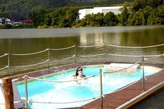 a woman is in an outdoor hot tub on a dock next to the water and trees