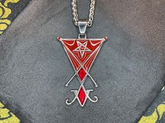 Embrace the enigmatic allure of the Sigil of Lucifer Pendant Necklace, adorned with striking red enamel and gleaming gemstone accents. Crafted from durable stainless steel, this necklace encapsulates the essence of the Seal of Satan. At its heart lies the potent Sigil of Lucifer, symbolizing enlightenment, defiance, and the pursuit of higher knowledge. Encircled by a mesmerizing pentagram, this pendant exudes an aura of mystique and power. Each pendant is meticulously crafted, with attention to Symbolic Red Pendant Jewelry, Symbolic Red Pendant Necklace, Satanic Jewelry, Sigil Of Lucifer, Inverted Pentagram, Gemstone Pendant Necklace, Gemstone Necklace Pendant, Gemstone Pendant, Jewelry Gift