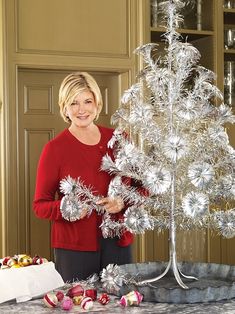 a woman standing next to a silver christmas tree