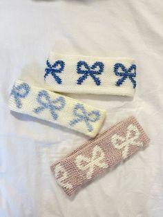 two knitted headbands with blue bows and numbers on them sitting on a white sheet