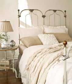 a bed with white linens and pillows in a bedroom next to a lamp on a table