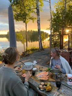 two women sitting at a picnic table with food on it and the sun setting in the background