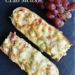 two pieces of bread sitting next to grapes on a slate platter with the words quick and easy crab melts