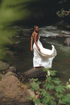 a woman in a white dress is standing on rocks by the water